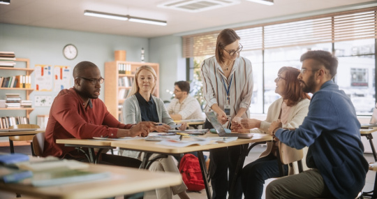 Educators confer with one another in an empty classroom.